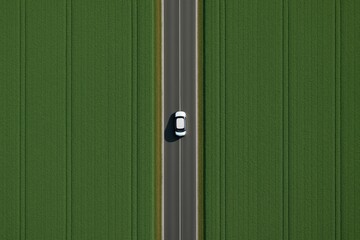 Fototapeta premium White car driving on straight road through green fields