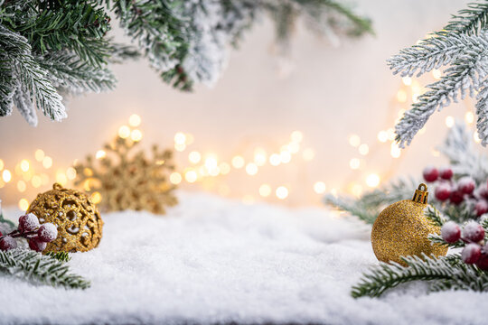 Glittering gold ornaments and snowflakes rest on snowy ground with frosted pine branches and soft glowing lights. Winter Christmas Holiday Decoration Background