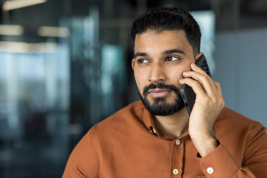 Indian businessman having a serious phone conversation, listening intently to the speaker while holding smartphone to ear in a modern office environment - Powered by Adobe