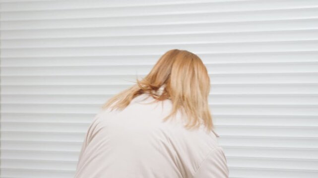 Back view of woman owner bending to roll up steel shutter of laundry room, hair moving, motion blur, indoor corridor setting, morning routine as lights come on, equipment faint in background