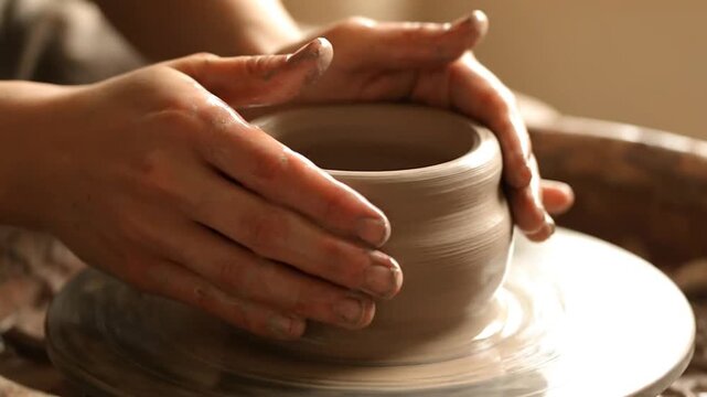 Artisan potter shaping a clay bowl on a wheel in a sunlit studio with tools and materials nearby