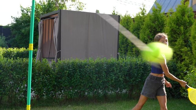 Young girl enjoys energetic outdoor games in sunny backyard, playing both badminton and tetherball