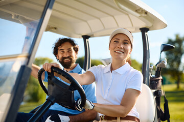 Happy couple of golfers driving golf cart on course.