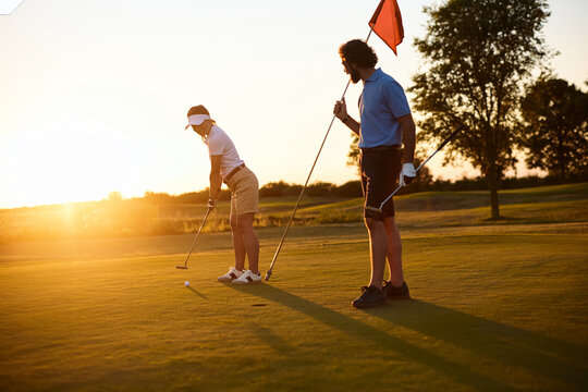 Female player aiming for hole on golf course at sunset. - Powered by Adobe