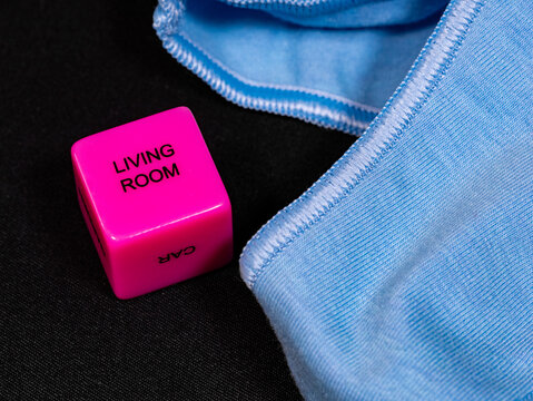 A playful close-up composition featuring a pink dice labeled “Living Room” and “Car” next to light blue clothing on a black surface.