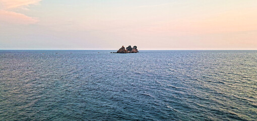 Tranquil seascape at sunset with a small rocky island covered in trees in the distance, surrounded by calm blue waters under a pastel sky. Petrovac, Montenegro-