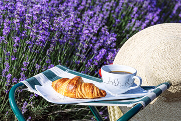 French breakfast with croissant and coffee served in a lavender field, France. A straw hat and basket add charm, symbolizing summer, travel, and countryside relaxation. © Natalya