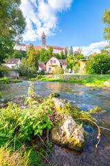 Charming riverside village with green hills, rocks along the river, and a tall castle church tower
