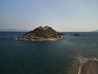 Aerial view of a small rocky islet with a Turkish flag and a curved sand spit on the Aegean coast of Mugla Province Turkey, warm light over calm water, quiet landmark for coastal walks and snorkeling