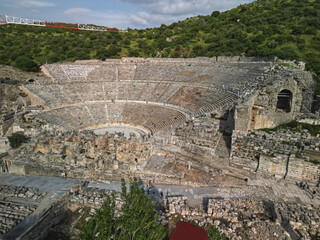 Aerial view across the great theatre at ephesus, stone rows climb the hillside, the ruined stage buildings fill the center, grand scale shows roman urban life in Turkey and lasting appeal