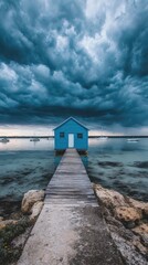 A serene, cobalt blue boathouse sits on a pier extending into a tranquil bay, framed by dramatic, brooding clouds.