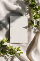 Minimalist blank card on soft fabric background with green leaves and natural sunlight, ideal for wedding invitations, branding, or elegant stationery mockups.
