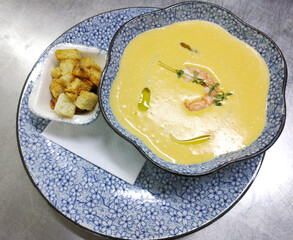 Creamy seafood soup with shrimp and croutons. The center of the soup is garnished with shrimp, sprigs of fresh herbs, and a drizzle of olive oil for a flavorful finish.