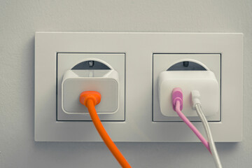 phone chargers and their cords plugged into the wall socket