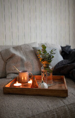 Cozy composition with cup of tea on the wooden tray, interesting book, candles and warm blanket. Hygge home interior.
Vertical image.
