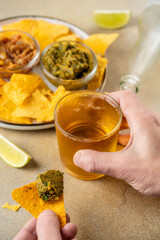 Hand holding beer and tortilla chip with dip on stone table