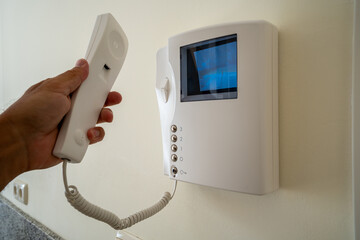 Hand holding intercom handset near video screen security device on wall in apartment