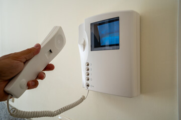 Hand holding intercom handset near video screen security device on wall in apartment