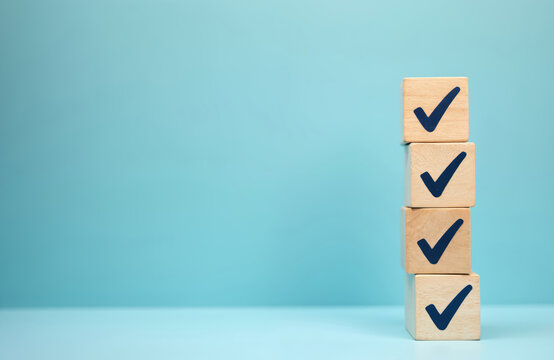 Stack of wooden blocks with check marks. Represents task completion, business survey, or exam success. Offers copy space on blue background for checklist, questionnaire, or form. - Powered by Adobe