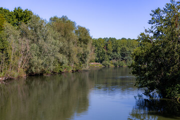 River with trees reflecting in calm water under blue sky