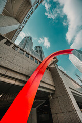 Naklejka premium A low-angle shot of the Tokyo Metropolitan Government Building complex, framed by a striking red, curved sculpture and modern architectural details
