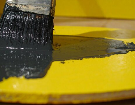 Paintbrush dipping into dark gray paint on a yellow palette