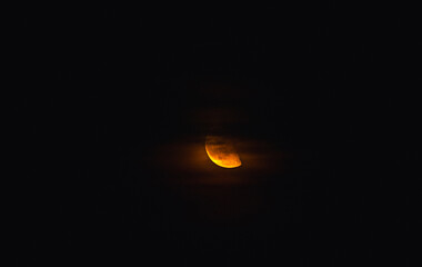 A glowing half moon, a warm orange light in the dark sky, partially obscured by the faint cloud.