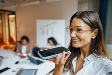 A professional woman effectively utilizing voice command technology on her smartphone in a modern office environment