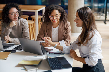 In a stylish office space, three women are actively engaged in a productive collaborative work...