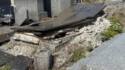 A destroyed grave in a cemetery, with a broken granite tombstone, crumbled concrete, and exposed rebar
