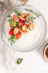 Appetizing overhead shot of a white frosted cake topped with fresh strawberries and elegant eucalyptus, with cocoa powder nearby