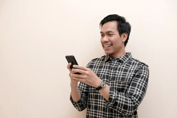Fototapeta premium Southeast Asian man wearing flannel shirt standing and smiling expression happy with holding mobile phone, on white isolated background.