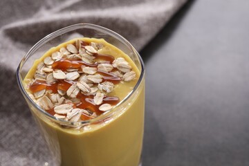 Glass of delicious smoothie with oat flakes and caramel syrup on grey table, closeup. Space for text