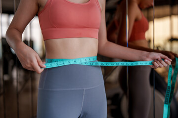 Woman measures her waist with tape measure in gym setting, focusing on fitness and wellness. This exercise reflects her commitment to self care and personal health