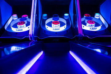 Close-up view of a skee-ball arcade game illuminated with neon blue and purple lights, capturing a fun and nostalgic carnival atmosphere.