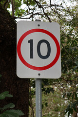 10 Kilometres Per Hour speed limit sign attached to a metal pole in front of a tree