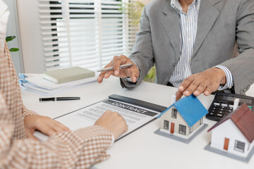 A real estate agent and client are discussing property purchase options, reviewing a contract, calculating loan terms, and considering house models as part of a housing investment decision.