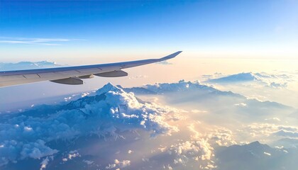 Obraz premium Aerial View of Airplane Wing Above Cloudscape During Sunrise with Golden Sunlight and Blue Sky Scenery
