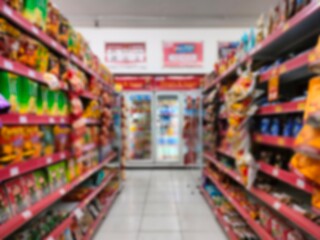 Blurred view of supermarket aisle with colorful packaged products on shelves. Grocery store interior background with snacks, food, and retail items for consumer and shopping concepts