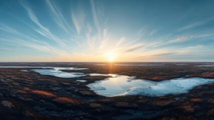 Fototapeta premium Frozen tundra landscape at sunset. Vast expanse of icy ponds and dark ground. Sunlight streaks across light clouds