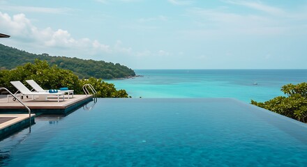 Fototapeta premium a infinity pool at a tropical resort with two empty,pristine white lounge chairs at the edge.The pool water is a deep blue blending seamlessly with the view of the turquoise ocean,a lush green 