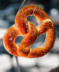 A freshly baked salted pretzel hangs elegantly in front of a blurred background.