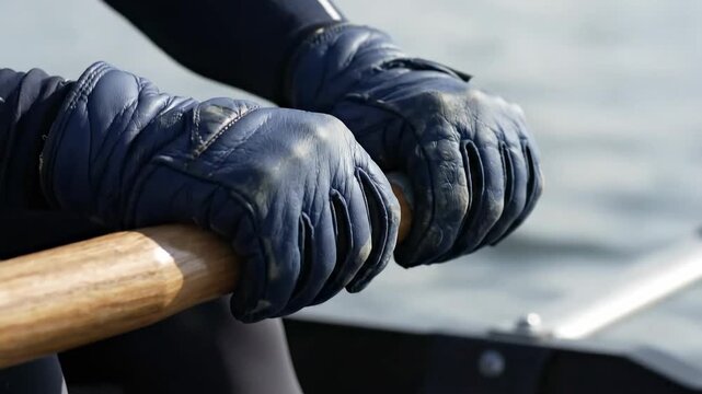 Close up of rower hands in gloves holding an oar on water.