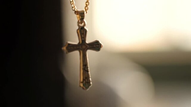 A close-up shot of a golden cross pendant hanging, illuminated by natural light.