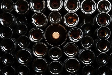 top view of multiple dark glass bottles closely arranged with one bottle centered with a cork, creating a pattern of circular reflections and shadows