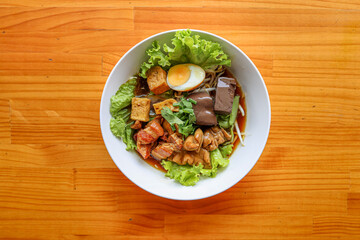 Savory Noodles Delight: A delectable Asian noodle dish is artistically presented in a white bowl. The ingredients are artfully arranged against the backdrop of a warm, wooden surface.