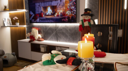 Warm Christmas living room with glowing candles, festive decorations, and cozy holiday ambiance in front of a TV fireplace.