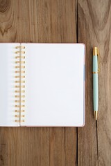 Minimalist top view of open spiral notebook with blank white pages and elegant mint green pen on natural wooden desk surface, symbolizing creativity, planning, writing, journaling, and productivity wo