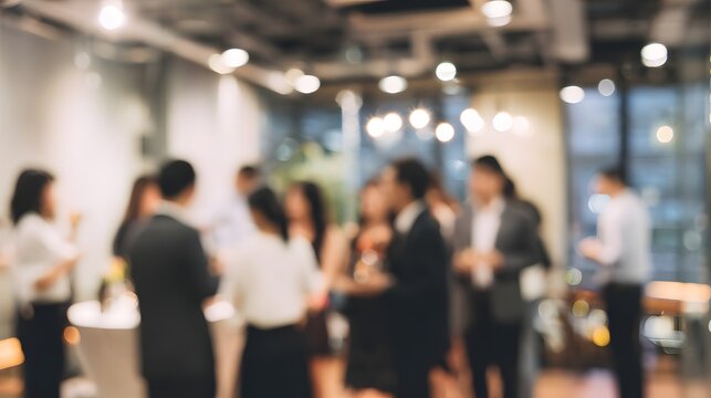 A blurred image of a social gathering or networking event, with people mingling and holding drinks in a modern indoor setting