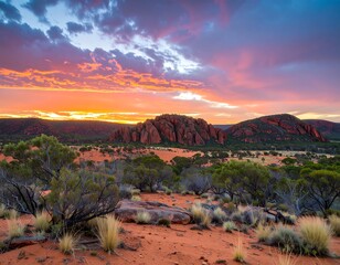 Vibrant sunset over desert landscape, red sand, shrubs, and rocky hills